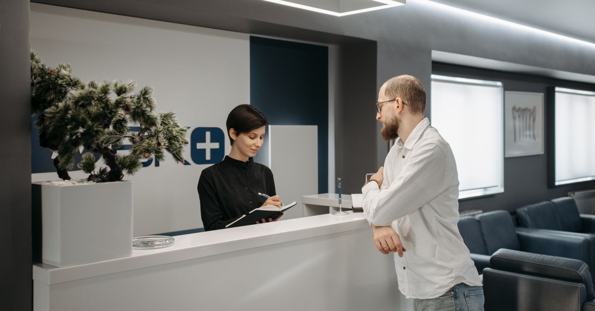 Patient checking in with a receptionist at a modern clinic front desk.